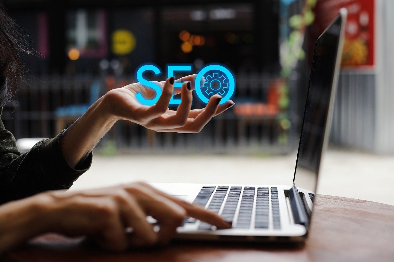 Mini SEO Audit helps to improve website visibility shown with a woman's hand holing the letters SEO while her other hand is typing on a laptop
