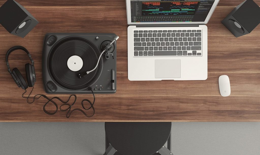 Ariel view of an open laptop on a dark wooden desk next to a record player, mouse and headphones