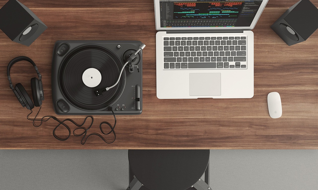 Ariel view of an open laptop on a dark wooden desk next to a record player, mouse and headphones