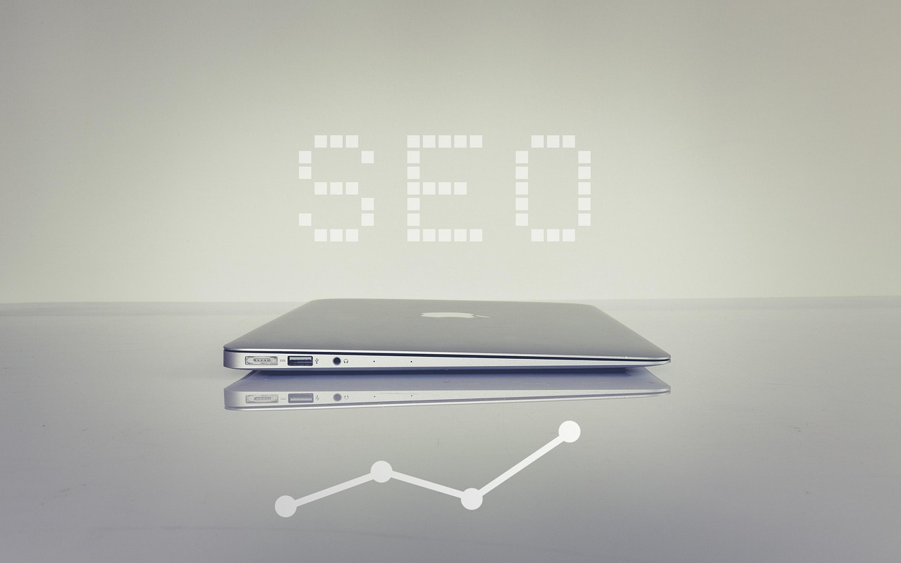 SEO letters above a closed silver laptop on a grey desk with a white graph graphic underneath