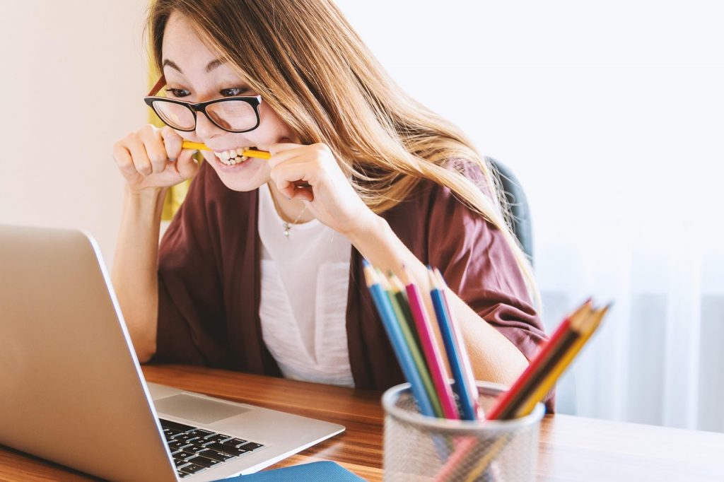 Female wearing glasses biting on her pencil in frustration, staring at her laptop screen