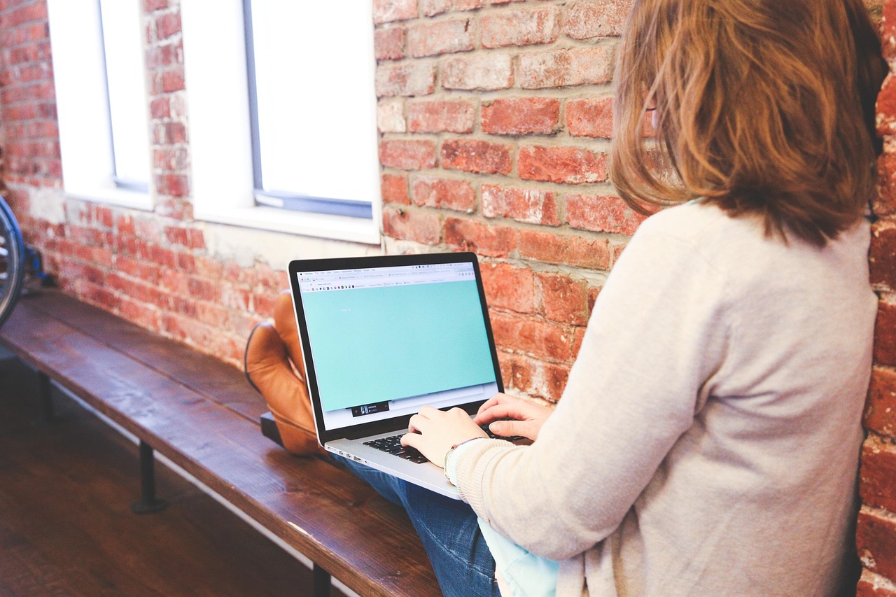 A woman sitting on a bench against a wall, typing on her laptop creating SEO-led content